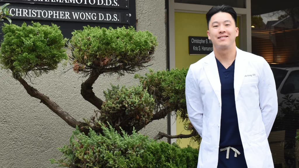 Dr. Christopher B. Wong in a white coat at the office entrance, beside the practice sign